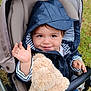 toddler, child, stroller, teddy_bear, hooded_jacket, smiling, waving, outdoor, grass, toy, baby, person, cute, happy, seat, clothing, hand, face, portrait, baby_carriage
