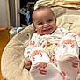 baby, infant, smile, pajamas, crab_pattern, baby_chair, plush, indoor, happy, cute, child, person, cozy, toothy_grin, comfortable, clothing, footed_pajamas, furniture, home, relaxed