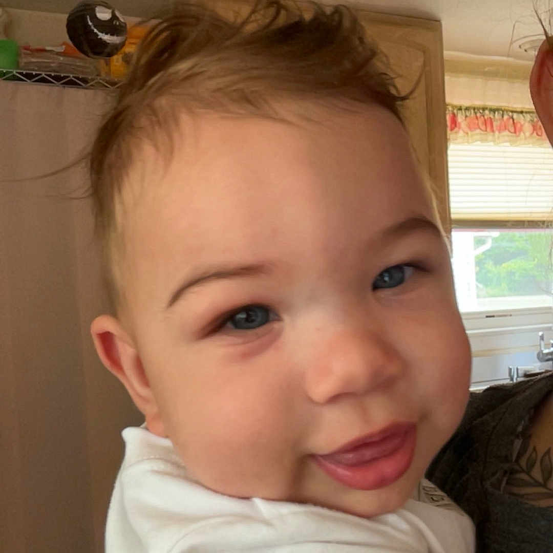 Karri joined the competition — help win amazing prizes! baby, child, infant, portrait, close_up, smiling, tongue_out, blue_eyes, brown_hair, white_shirt, being_held, adult, indoor, kitchen, window, shelves, home, warm_lighting, happy, face