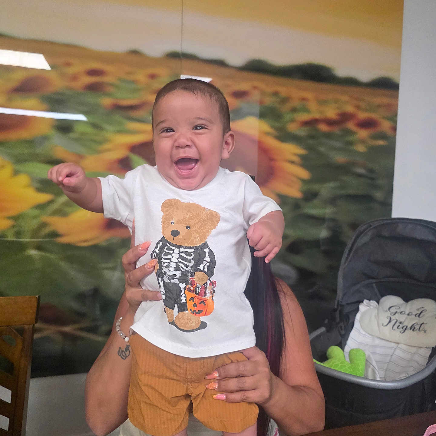 Emiliano joined the competition — help win amazing prizes! baby, child, infant, smiling, laughing, portrait, held, adult, tshirt, teddy_bear, shorts, shoes, stroller, pillow, sunflower, indoor, home, furniture, happy, photography