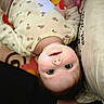 baby, infant, face, upside_down, onesie, floral_pattern, cushion, soft_fabric, indoor, child, skin, head, expression, curious, person, closeup, cute, smile, baby_clothing, resting