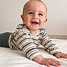 baby, child, smiling, lying_down, striped_shirt, hands, face, happy, infant, cute, indoor, bed, white_bedspread, portrait, young_child, skin, person, casual_clothing, head, eyes