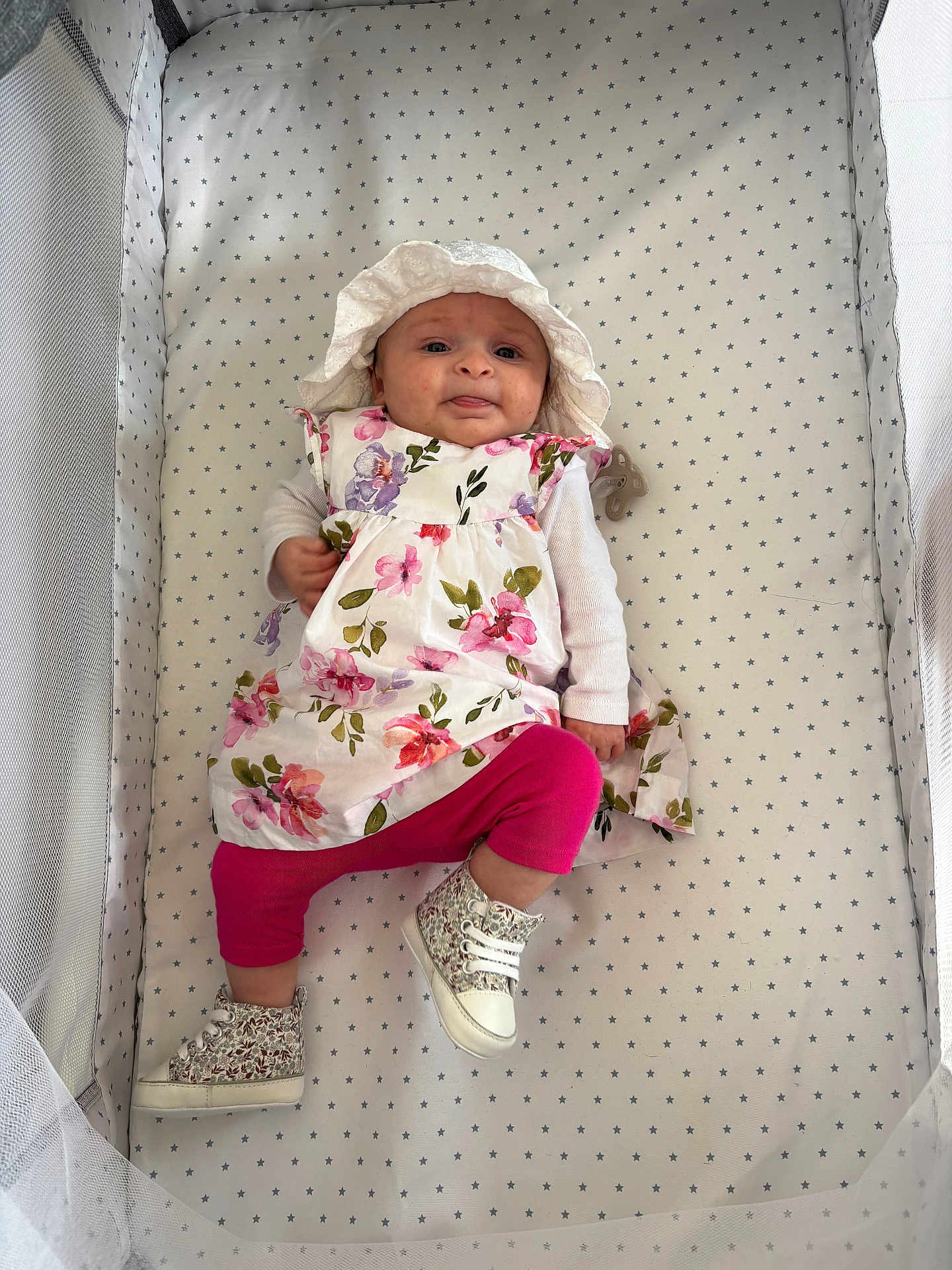 Juliette a rejoint le concours — aidez-le/la à gagner de superbes lots ! baby, infant, crib, floral_dress, hat, pink_leggings, boots, face, tongue_out, patterned_bedding, mesh_sides, cute, child, lying_down, playful, indoors, person, apparel, footwear, smiling