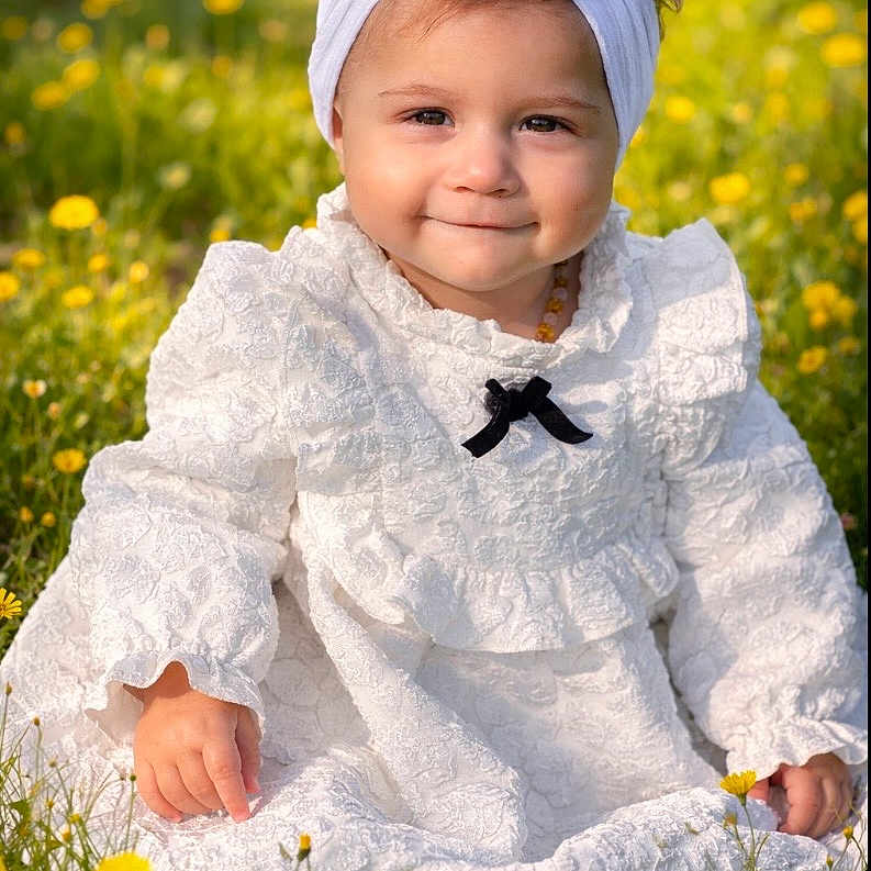 Léana participe au concours pour gagner de l'argent avec cette photo : toddler, child, white_dress, headband, bow, smiling, outdoor, flowers, meadow, grass, sunlight, portrait, baby, cute, nature, sitting, young_child, yellow_flowers, happy, innocence