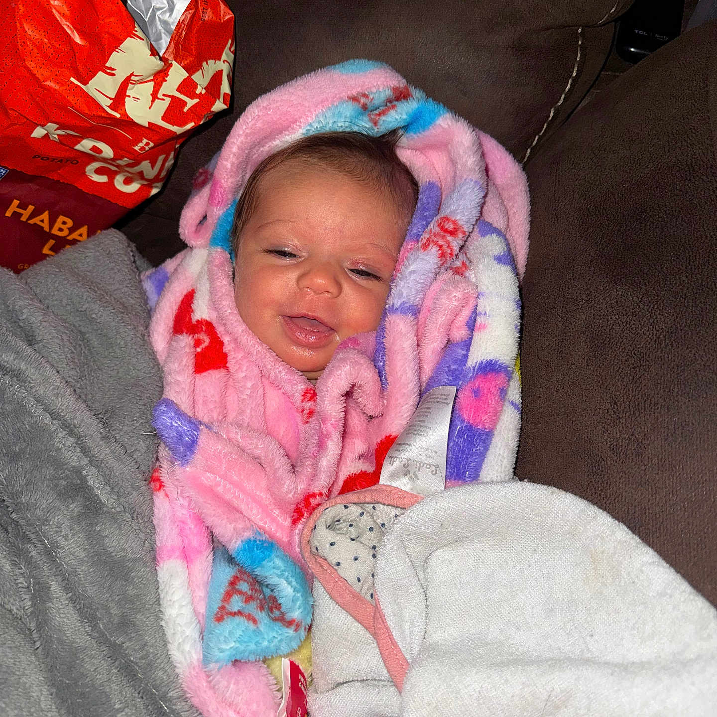 Harper joined the competition — help win amazing prizes! baby, blanket, smiling, couch, indoor, child, face, colorful, cozy, fabric, person, happy, wrapped, soft, home, relaxed, snug, infant, plush, casual