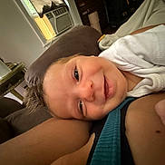 Harper is registered to the contest to win money with this photo: baby, smile, face, arm, indoor, couch, fan, air_conditioner, blanket, clothing, person, happy, head, resting, skin, comfort, closeup, toddler, relaxation, home