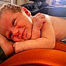 Harper is registered to the contest to win money with this photo: baby, infant, smile, face, skin, hand, arm, diaper, lying_down, closeup, person, cute, newborn, resting, indoors, soft_lighting, orange, warm, cozy, portrait