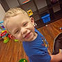 child, boy, smiling, blonde_hair, blue_shirt, toy, playroom, wooden_floor, shelf, plastic_toys, indoor, happy, cute, preschooler, person, young_child, floor, colorful, play, casual_clothing
