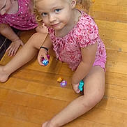 Jule is registered to the contest to win money with this photo: child, children, girl, floor, wooden_floor, toy, playing, indoor, casual, pink_clothing, pigtails, curly_hair, barefoot, book, colorful_toy, smile, sitting, person, young, playtime