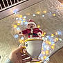 baby, child, christmas, cute, decor, fairy_lights, festive, floor, hand, holiday, indoor, person, red, rug, santa_costume, smiling, teacup, toy, white, yellow