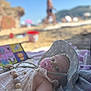 baby, beach, blanket, child, clothing, cute, daytime, hat, infant, lying_down, outdoor, pacifier, portrait, relaxing, sand, summer, sunhat, sunny, toy, vacation