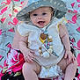 baby, blanket, child, clothing, cute, daisy_pattern, diaper, flamingo_pattern, happy, hat, infant, lap, outdoor, person, playful, skin, smiling, summer, watermelon_pattern, wooden_beads