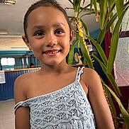 Hayden a rejoint le concours — aidez-le/la à gagner de superbes lots ! child, girl, smiling, portrait, indoor, knitted_top, earrings, plants, greenery, face, person, casual_clothing, happy, young, cute, hair_tied, background, light, beads, decor
