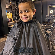 Sohan participe au concours pour gagner de l'argent avec cette photo : child, boy, smile, haircut, barbershop, cape, black_cape, hair, chair, interior, mirror, lighting, portrait, happy, person, indoor, fashion, cute, hairstyle, studio