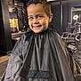 child, boy, smile, haircut, barbershop, cape, black_cape, hair, chair, interior, mirror, lighting, portrait, happy, person, indoor, fashion, cute, hairstyle, studio