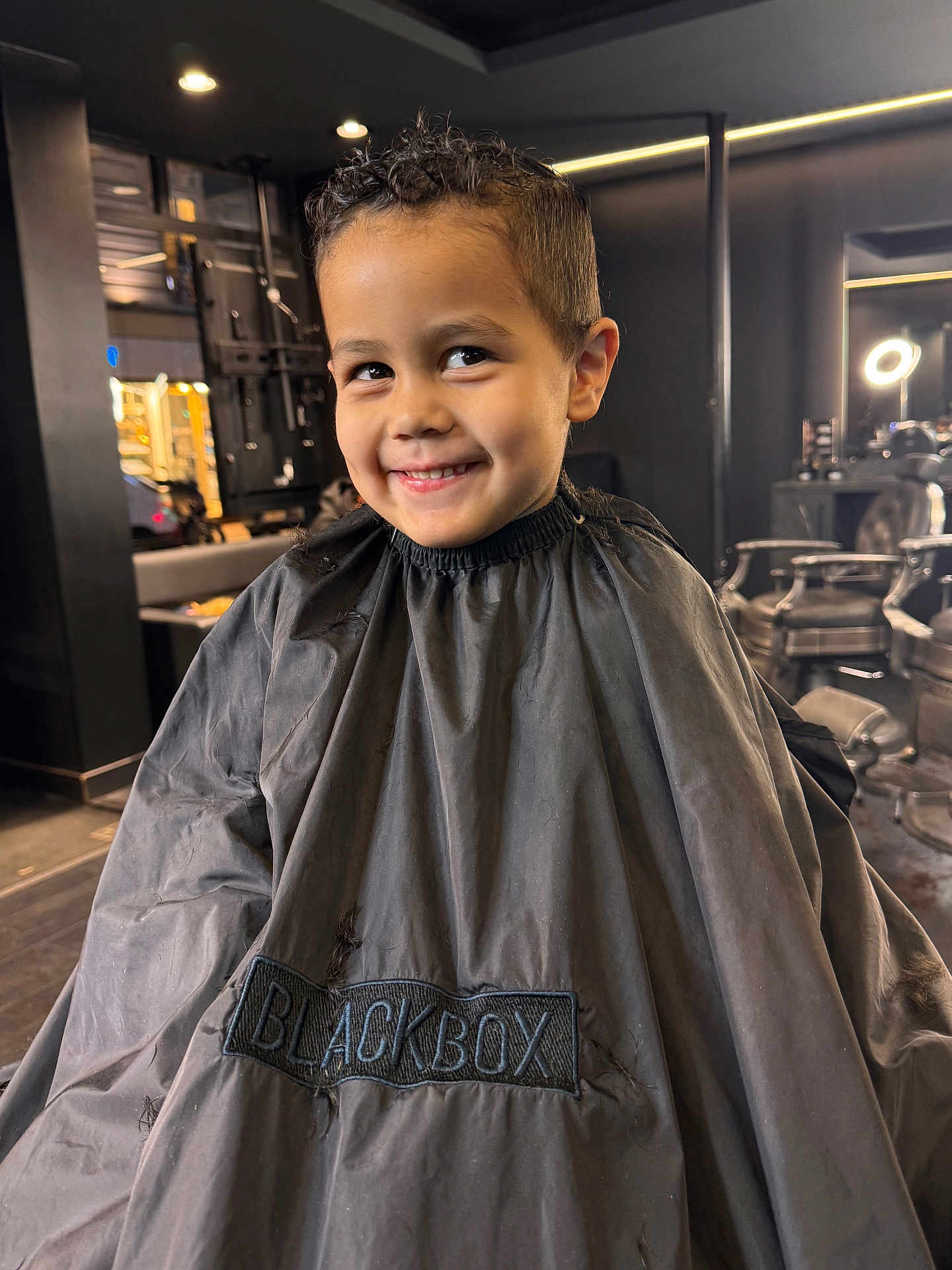 Sohan participe au concours pour gagner de l'argent avec cette photo : child, boy, smile, haircut, barbershop, cape, black_cape, hair, chair, interior, mirror, lighting, portrait, happy, person, indoor, fashion, cute, hairstyle, studio