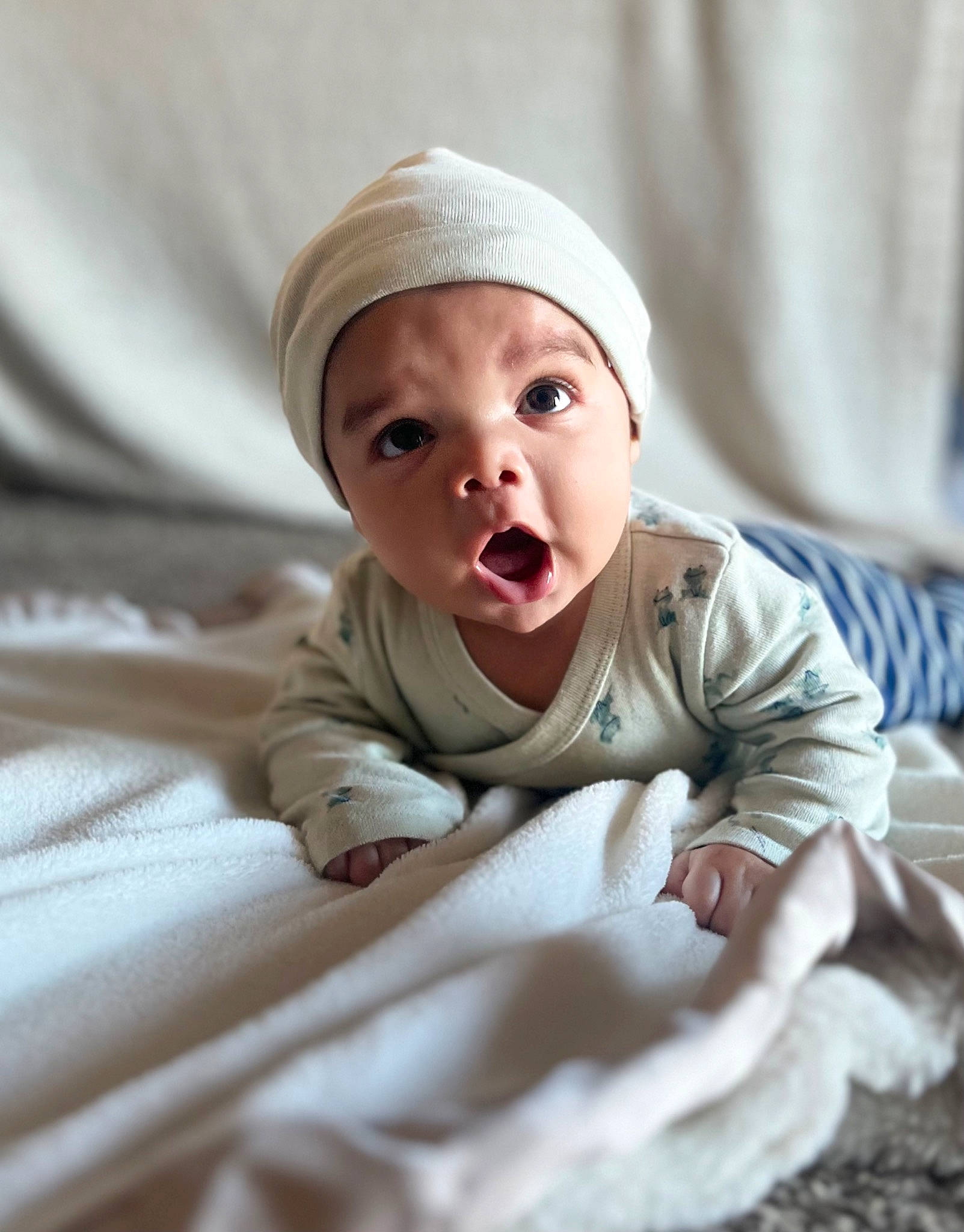 Kai is registered to the contest to win money with this photo: baby, baby_toddler_clothing, bed_sheet, bedding, child, comfort, flooring, happy, headwear, linens, person, portrait_photography, room, sitting, sleeve, toddler, wood