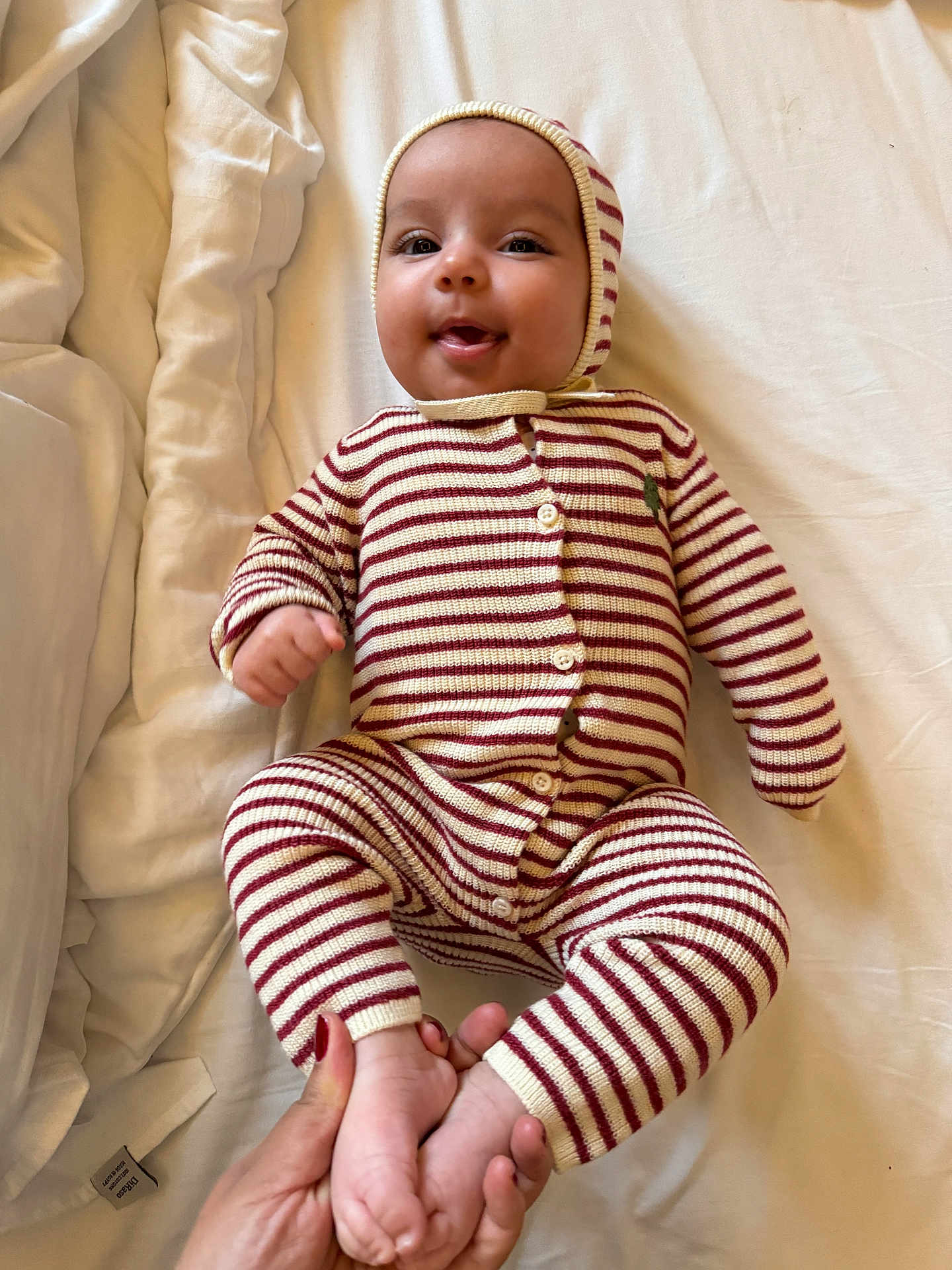 Eline a rejoint le concours — aidez-le/la à gagner de superbes lots ! baby, infant, smiling, striped_clothing, onesie, hood, hand, feet, bed, blanket, white_background, cute, child, person, portrait, lying_down, soft_lighting, cozy, happy, tender_moment