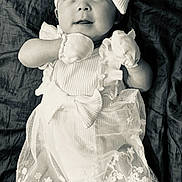 Emma joined the competition — help win amazing prizes! baby, infant, dress, bow, mittens, white_clothing, headband, portrait, laying_down, blanket, cute, child, smiling, soft_lighting, monochrome, fabric, young, expression, socks, newborn