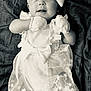 baby, infant, dress, bow, mittens, white_clothing, headband, portrait, laying_down, blanket, cute, child, smiling, soft_lighting, monochrome, fabric, young, expression, socks, newborn