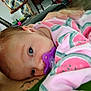 baby, pacifier, infant, close_up, pink_clothing, watermelon_print, tattoo, green_clothing, face, resting, indoor, adult, hand, water_bottle, fabric, pattern, person, skin, head, sleepy