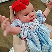 Jazmine is registered to the contest to win money with this photo: baby, infant, child, red_bow, blue_dress, tattoo, arm, hand, cute, indoor, wood_floor, person, face, smiling, holding, closeup, young, portrait, clothing, skin