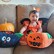 Havenayha is registered to the contest to win money with this photo: baby, child, halloween_costume, orange_dress, bat_wings, headband, pumpkin, black_cat_bag, trick_or_treat_bag, couch, indoor, smiling, cute, holiday, festive, decor, happy, sitting, toy, costume