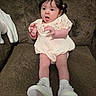 Azalea joined the competition — help win amazing prizes! baby, infant, child, couch, brown_couch, white_shoes, white_socks, cream_dress, pigtails, hair_buns, cute, surprised, indoors, plush, seated, portrait, young_child, people, person, expression
