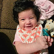 Azalea is registered to the contest to win money with this photo: baby, bib, brown_background, child, closeup, curly_hair, cute, hand, happy, indoor, infant, lying_down, pacifier, person, pink_clothing, plush_toy, portrait, smiling, soft_toy, toddler