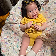 Azalea joined the competition — help win amazing prizes! baby, smiling, curly_hair, yellow_onesie, white_socks, blanket, patterned_blanket, child, indoor, happy, cute, infant, sitting, clothing, hair_clips, portrait, face, person, joy, toddler