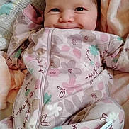 Charlotte is registered to the contest to win money with this photo: baby, smiling, onesie, floral_pattern, blanket, infant, cute, cozy, lying_down, soft, face, happy, child, newborn, sleepwear, indoors, comfort, person, portrait, closeup