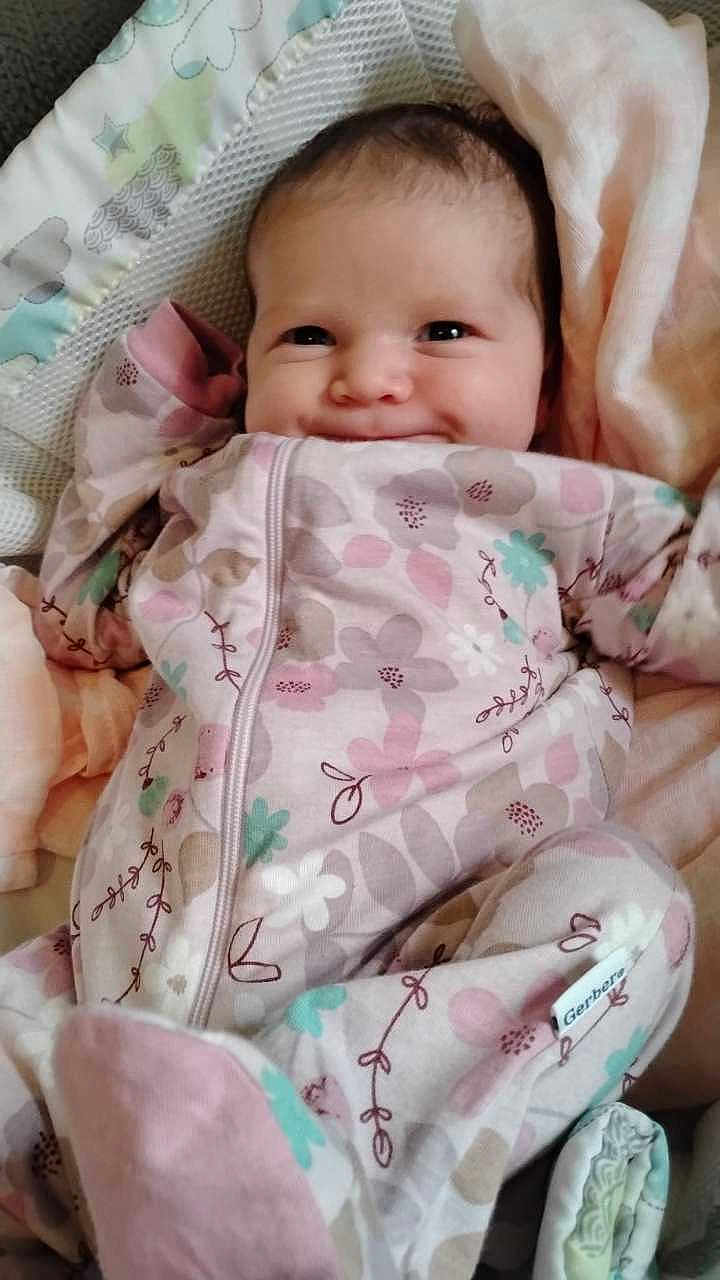 Charlotte is registered to the contest to win money with this photo: baby, smiling, onesie, floral_pattern, blanket, infant, cute, cozy, lying_down, soft, face, happy, child, newborn, sleepwear, indoors, comfort, person, portrait, closeup