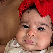 Ayla is registered to the contest to win money with this photo: baby, infant, child, portrait, close_up, face, eyes, red_bow, headband, floral_clothing, outfit, sofa, couch, indoor, cozy, reclining, looking_at_camera, photography, cute, soft_lighting