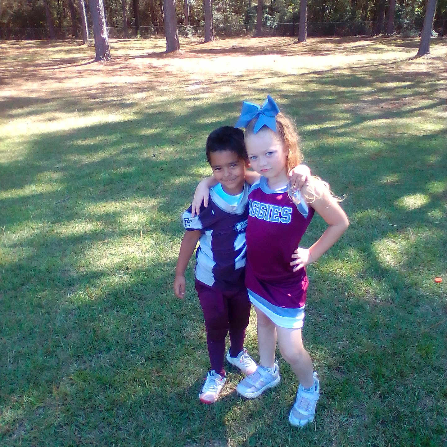 April is registered to the contest to win money with this photo: bow, cheerleader, child, children, daylight, field, football_uniform, friends, friendship, grass, outdoor, posing, serious, shoes, smile, sports, team, trees, uniform, young