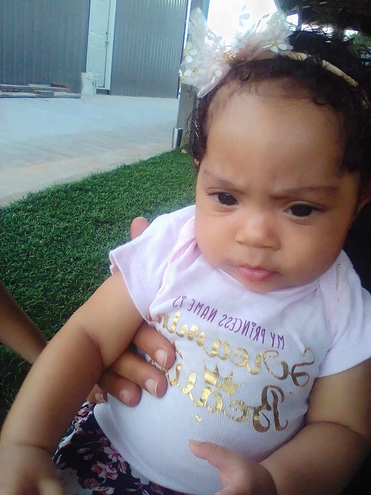 Mellissia joined the competition — help win amazing prizes! baby, child, infant, girl, headband, pink_shirt, outdoor, grass, hand, person, curly_hair, closeup, expression, cute, young, portrait, casual_clothing, skin, face, holding