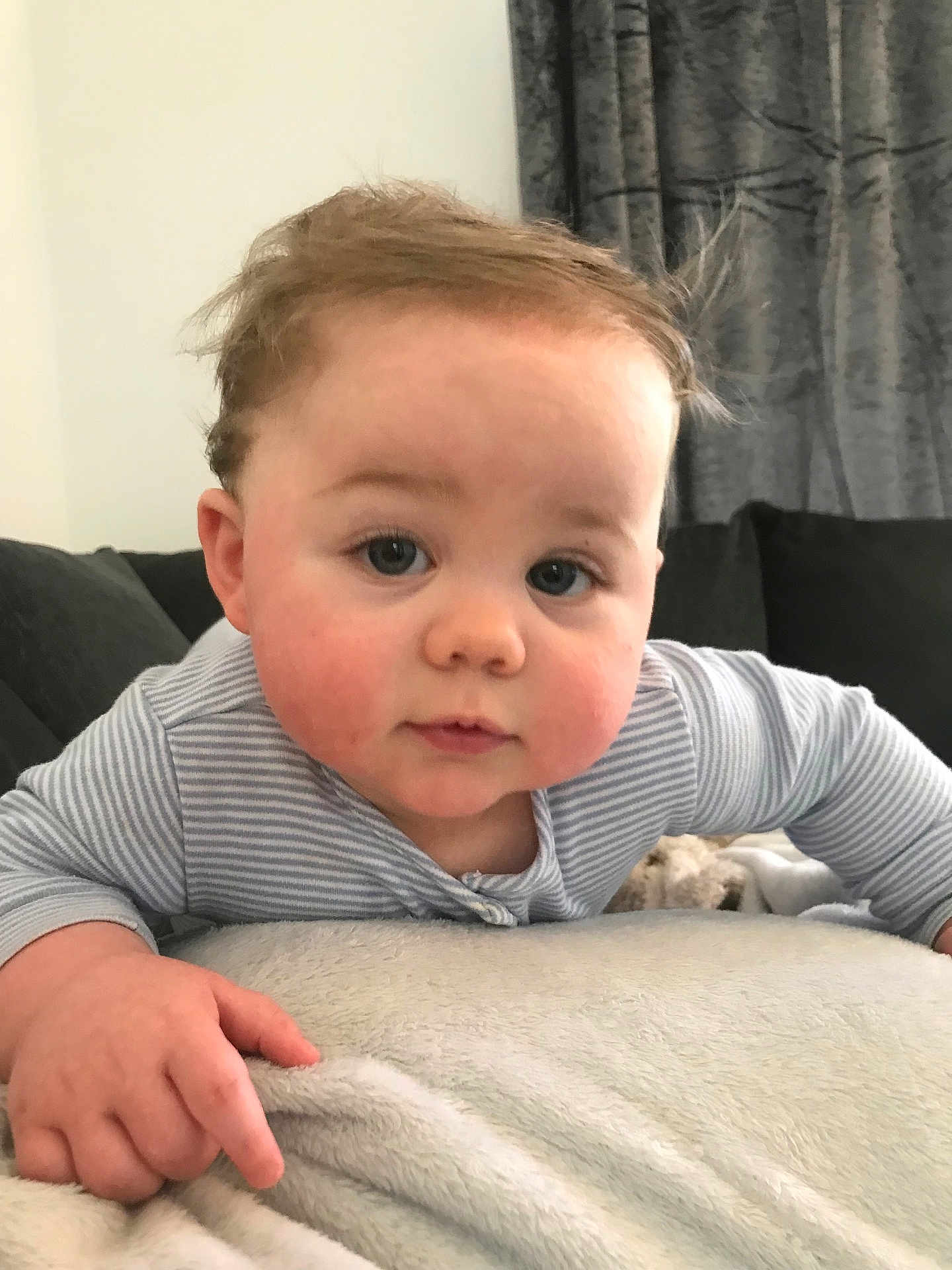Mason is registered to the contest to win money with this photo: baby, child, face, hands, blanket, couch, curtains, indoor, clothing, striped_shirt, rosy_cheeks, tousled_hair, soft_texture, portrait, infant, cute, person, closeup, home, expression