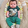 baby, infant, child, baby_chair, green_clothing, striped_socks, turtle_graphic, cute, indoors, floor, wooden_floor, patterned_fabric, seated, young_child, person, portrait, comfortable, expression, head, face
