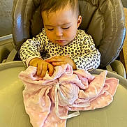 Nour participe au concours pour gagner de l'argent avec cette photo : baby, child, high_chair, blanket, soft_toy, pink, leopard_print, clothing, indoor, curly_hair, person, cute, toddler, table, exploring, facial_expression, seat, cozy, infant, hands