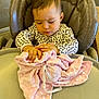 baby, child, high_chair, blanket, soft_toy, pink, leopard_print, clothing, indoor, curly_hair, person, cute, toddler, table, exploring, facial_expression, seat, cozy, infant, hands