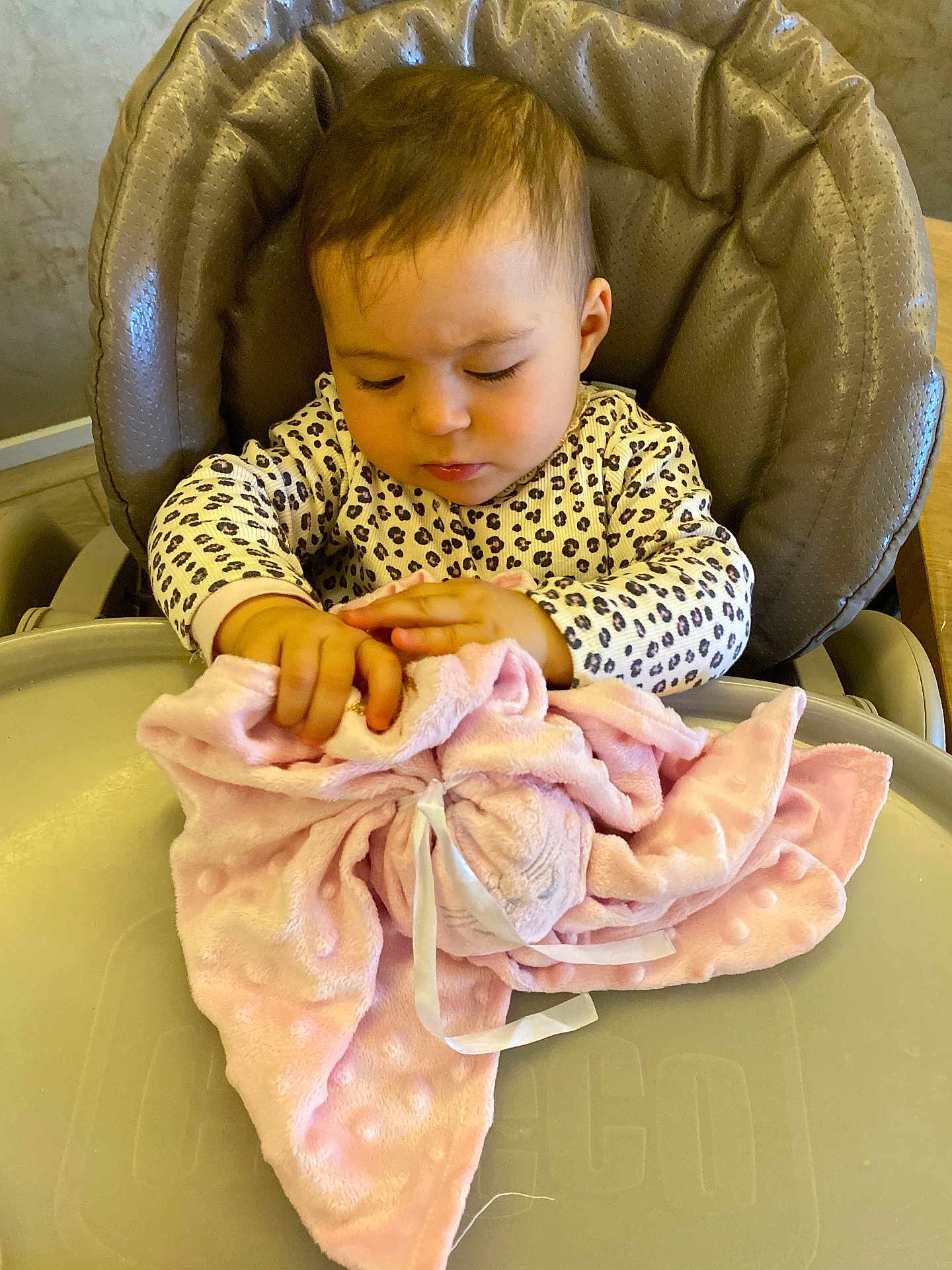 Nour participe au concours pour gagner de l'argent avec cette photo : baby, child, high_chair, blanket, soft_toy, pink, leopard_print, clothing, indoor, curly_hair, person, cute, toddler, table, exploring, facial_expression, seat, cozy, infant, hands
