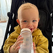 Ayden participe au concours pour gagner de l'argent avec cette photo : toddler, child, stroller, water_bottle, yellow_hoodie, blue_eyes, blond_hair, smiling, indoor, face, hand, clothing, cute, baby, person, seat, toy, playful, happy, portrait