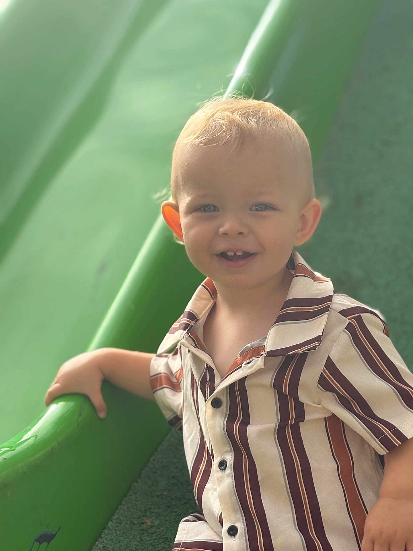 Ayden participe au concours pour gagner de l'argent avec cette photo : child, toddler, smiling, striped_shirt, blond_hair, blue_eyes, green_slide, playground, hand, short_sleeves, outdoor, happy, cute, casual_clothing, portrait, daylight, young_child, play, fun, kid