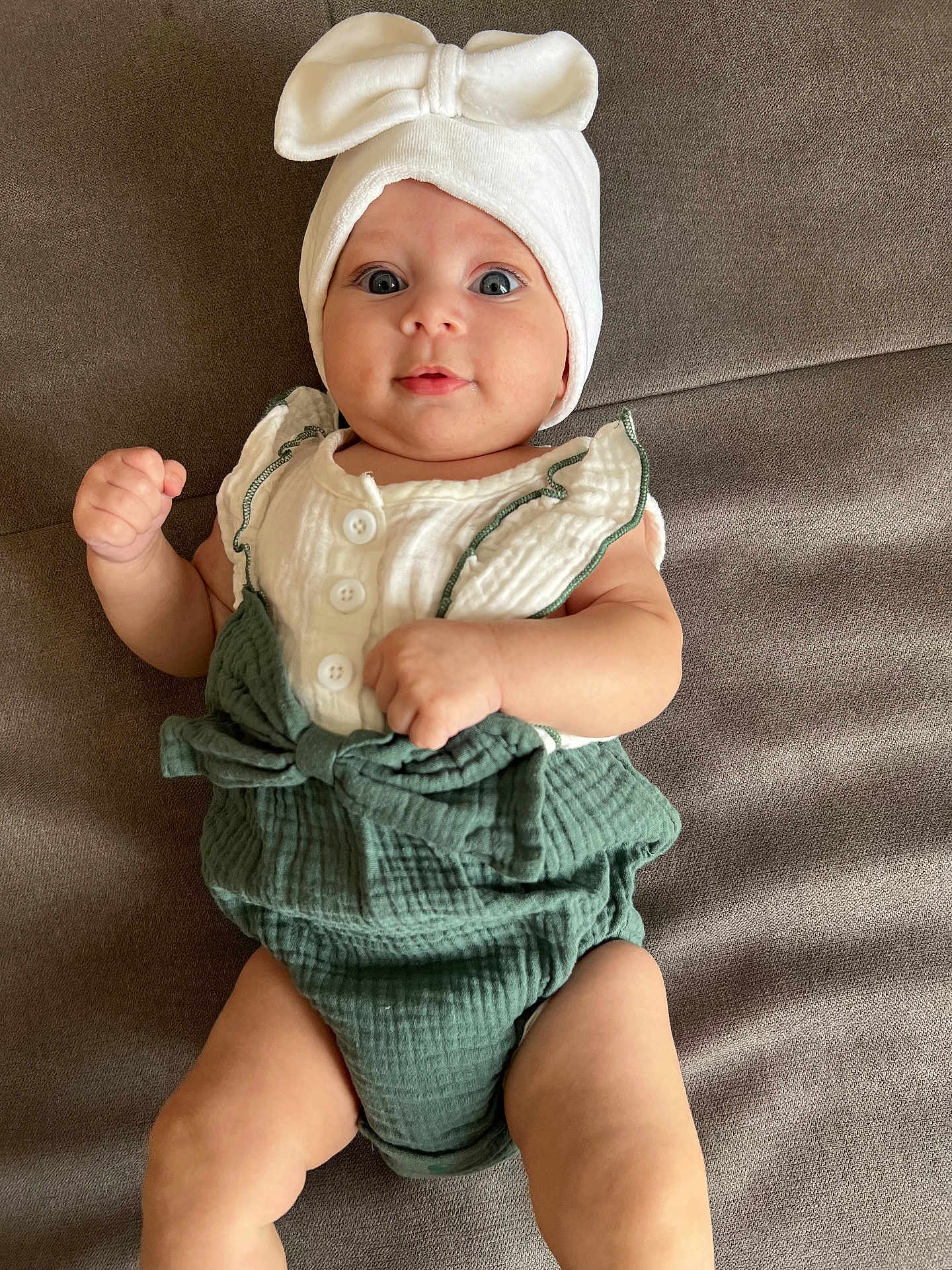 Naïssya participe au concours pour gagner de l'argent avec cette photo : baby, baby_fashion, bow, child, clothing, cute, eyes, gray_background, green_outfit, hands, headwrap, indoor, infant, legs, lying_down, portrait, skin, smile, soft_surface, white_top