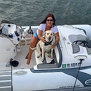 Katie is registered to the contest to win money with this photo: woman, dog, boat, water, sunglasses, smile, seat, bandana, outdoor, pet, yellow_labrador, casual_clothing, summer, steering_wheel, relaxation, recreation, vacation, happy, nature, transportation
