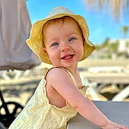 Imogen joined the competition — help win amazing prizes! baby, child, smiling, yellow_hat, yellow_dress, sunhat, outdoor, beach, table, blue_sky, portrait, happy, cute, infant, summer, sunny, daytime, closeup, person, leisure