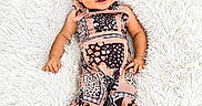 Hallie is registered to the contest to win money with this photo: baby, infant, smiling, black_bow, patterned_outfit, lying_down, fluffy_rug, white_background, cute, child, happy, portrait, adorable, fashion, headband, small_feet, skin, one_person, indoor, young_child