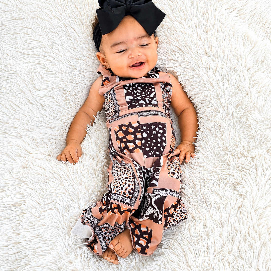 Hallie is registered to the contest to win money with this photo: baby, infant, smiling, black_bow, patterned_outfit, lying_down, fluffy_rug, white_background, cute, child, happy, portrait, adorable, fashion, headband, small_feet, skin, one_person, indoor, young_child