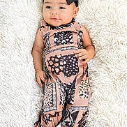 Hallie is registered to the contest to win money with this photo: baby, infant, child, black_bow, patterned_clothing, lying_down, fluffy_rug, white_background, cute, portrait, fashion, foot, hand, smile, indoors, soft_texture, young_child, headwear, person, comfortable