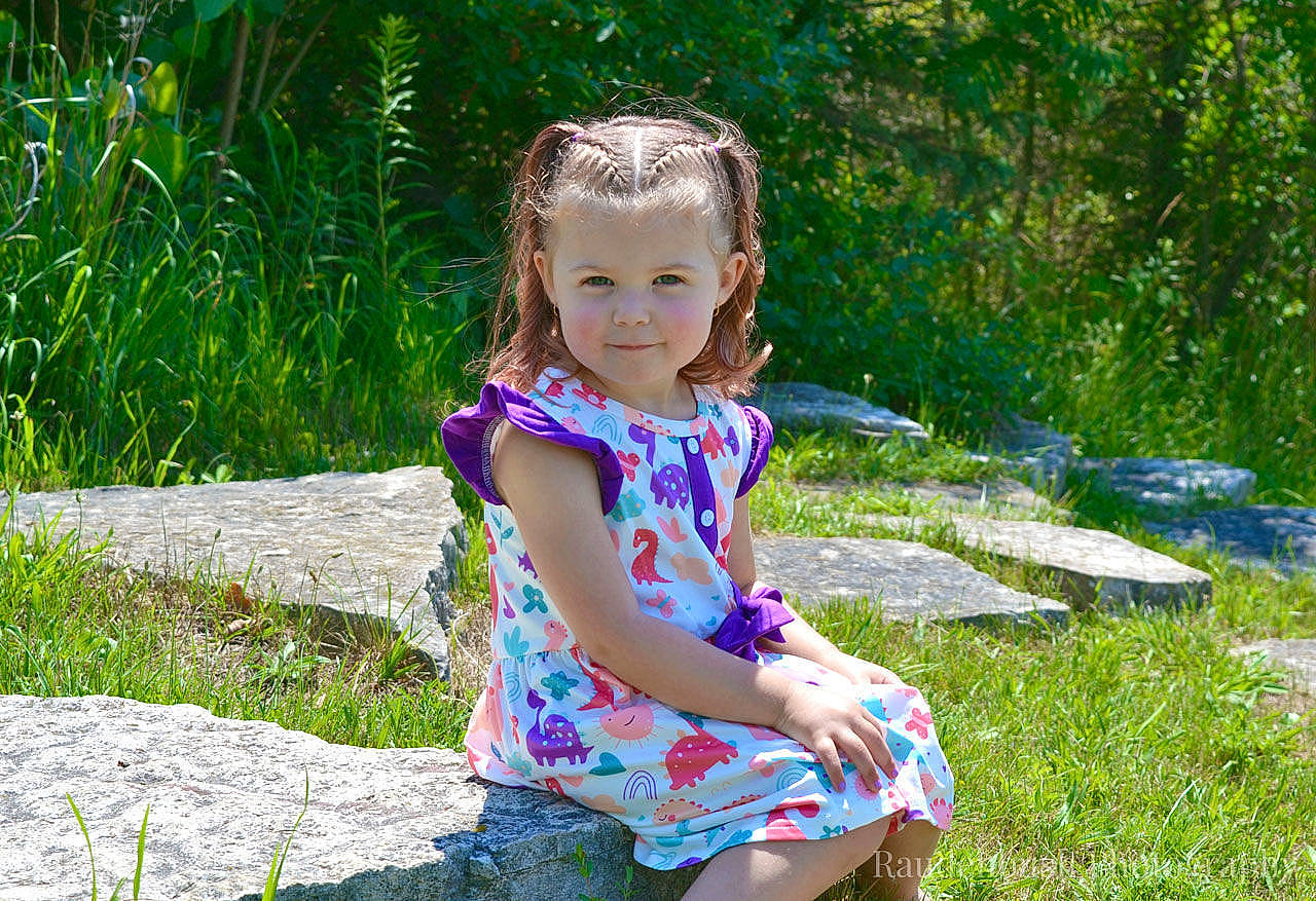 Daisy Jo is registered to the contest to win money with this photo: baby_toddler_clothing, child, dress, electric_blue, fun, grass, grassland, happy, leisure, meadow, pattern, people_in_nature, person, plant, recreation, sitting, spring, summer, sunlight, toddler