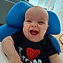 baby, black_shirt, blue_pillow, child, cute, furniture, hand, happy, high_chair, home, indoor, infant, light, person, portrait, red_heart, room, smiling, window, young_child